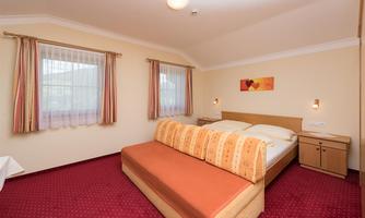 A cozy bedroom with a large double bed and red carpets. Bright curtains and a colorful wall decoration create an inviting atmosphere.