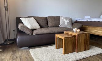 A cozy living room with a brown sofa and a pillow with an antler motif. Next to the sofa, there are three small wooden tables on a rug.