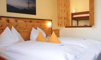 A cozy bedroom with a double bed and a loft bed. The walls are painted in soft colors, and there is a picture with a cross in the background.