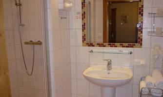 A modern bathroom with a spacious shower and a sink. Towels are neatly stacked on a shelf.