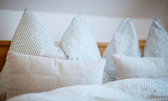 A cozy bed arrangement with decorative pillows in neutral colors. The pillows have different patterns and shapes.