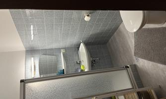 A modern bathroom with gray tiles and a shower area. There is a sink and a toilet, as well as some hygiene products on the shelf.
