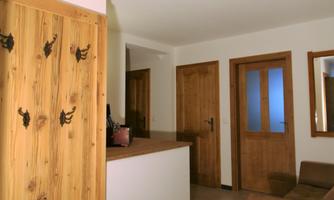 A modern hallway with wooden tiles and a clear design. On the left side, there is a wooden bench with hooks for coats.