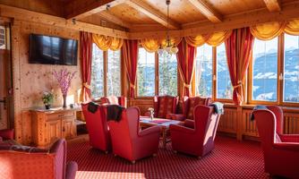 A cozy room with red armchairs and a large window that offers a view of the mountains. Wood paneling and warm colors create an inviting atmosphere.