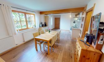 A cozy dining area with a wooden desk and chairs. Nearby, there's a bright kitchen with modern appliances and large windows.