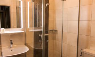 A modern bathroom with a glass shower and a sink. The tiles are light and the fixtures are functional.