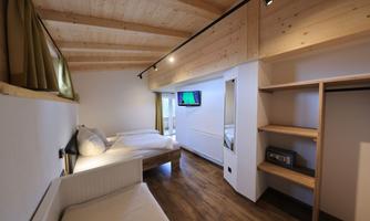 Bright room with wooden ceilings and a television on the wall. There is a single bed and a double bed as well as a wardrobe.