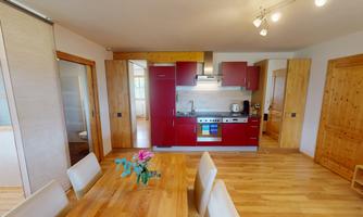 A modern kitchen with red cabinets and wooden flooring is visible. The dining area is bright and inviting with a table and chairs.