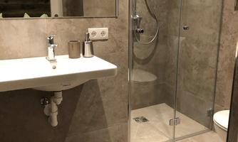 A modern bathroom with a glass shower cubicle and an elegant sink. The walls are designed with light tiles.