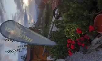 A cozy outdoor area with colorful flowers and a privacy screen. In the background, mountains and a cloudy sky can be seen.