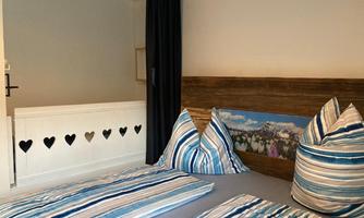 A cozy bedroom with two beds and striped pillows. The wall decoration features a mountain landscape, and the partition has heart-shaped cutouts.