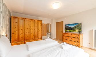 A cozy bedroom with two single beds. In the background, there is a wooden wardrobe and a television.