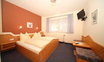 A cozy bedroom with two beds and wooden paneling. The room has a window with curtains and a TV on the wall.