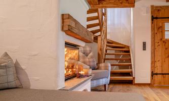 A cozy living space with a fireplace and a wooden staircase. The room has a warm, inviting feel.