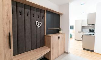 A modern entrance area with a wooden bench. In the background, an open kitchenette can be seen.