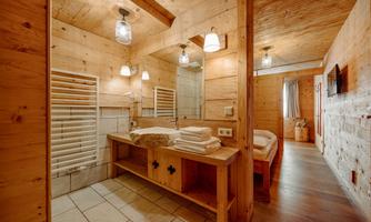 A modern wooden bathroom with bright lighting. There is a large sink, towels, and a mirrored wall cabinet.