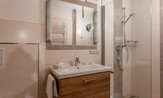 A modern bathroom with a shower and a wooden sink. The walls are painted in soft colors and there is a large mirror.