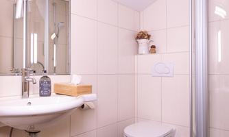 A modern bathroom with a sink, a toilet, and a shower. The walls are brightly tiled and there are decorative elements on the shelf.
