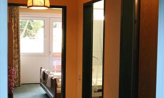 A short hallway with doors to rooms. On the left side, there is a window with curtains, and a part of the room is visible.