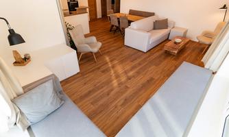 A modern living room with wooden flooring and cozy seating. The space is bright and pleasantly designed, ideal for relaxation and social gatherings.