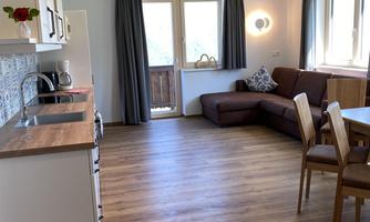 A bright, modern apartment with a kitchenette and a cozy living area. Large windows provide plenty of natural light and a view outside.