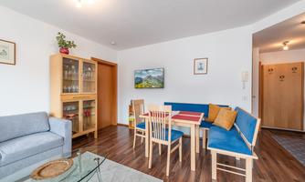 A cozy living room with a couch and a dining table. The walls are light, and there are pictures as well as a display cabinet.