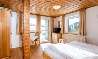 A cozy bedroom with wood paneling and large windows. The room is bright and welcoming, with a small table and a television.