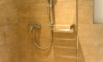 A modern shower with brown tiles and chrome fixtures. The showerhead is adjustable and the shower has an elegant glass enclosure.
