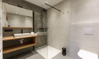 A modern bathroom with a glass shower and a wooden shelf. It features an elegant sink and toilet combination in neutral colors.