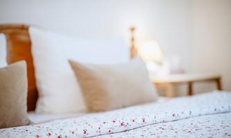A cozy bed with floral bedding and soft pillows. Next to the bed is a table with a lamp.
