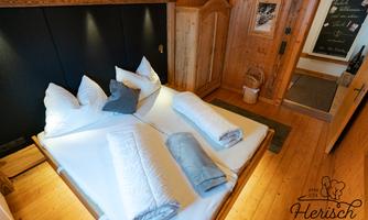 A cozy bedroom with a large double bed and fresh bedding. The wooden details and soft lighting create a warm atmosphere.