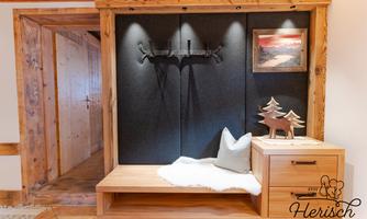 A cozy entrance area with a wooden bench and a decorative cushion. On the wall hang some decorative items and a picture.