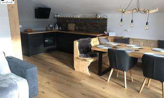 A modern kitchen with wooden details and a dining area made of wood and black chairs. The room has bright walls and a cozy look.