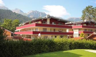 Modern residential buildings surrounded by green spaces and mountains in the background. The architecture is colorful and harmoniously integrated into the landscape.