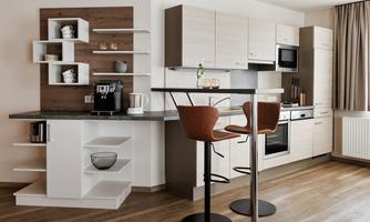 Modern kitchen with light cabinets and an elegant countertop. A cozy dining area with two bar stools and a coffee machine.