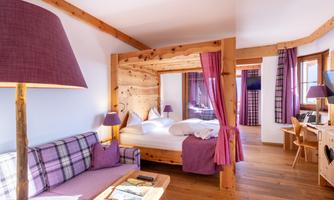 A cozy hotel room with a four-poster bed and wooden elements. The warm colors and modern furnishings create an inviting atmosphere.