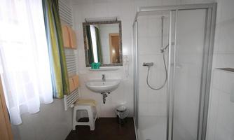 A modern bathroom with a shower, a sink, and a mirror. The walls are brightly tiled, and there are fresh towels in orange and green colors.