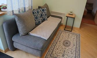 A cozy sofa with large cushions and a blanket. Next to it stands a small table and a decorative rug lies on the floor.