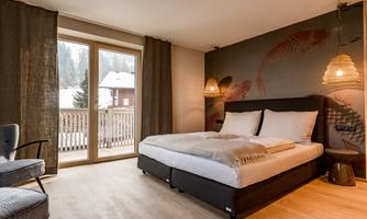 A modern bedroom with a large bed and elegant details. Large windows offer a view of the surroundings.