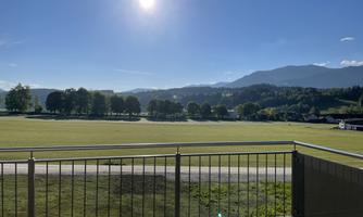 A beautiful view from a balcony of a green meadow and gentle hills in the background. The sky is blue and the sun is shining.