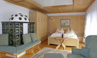 A cozy bedroom with a double bed and wood paneling. A charming seating area and a traditional tiled stove give the room a homely atmosphere.