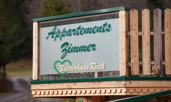 A sign for an apartment building with the inscription "Apartments Rooms" in a quiet, rural area. It is surrounded by nature and wood.