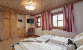 A cozy bedroom with wooden walls and a large window. There is a double bed, a TV, and a rustic wooden dresser.