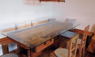 A stylish dining area with a wooden table and transparent glass protection. Around the table are wooden chairs with soft cushions.