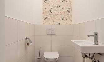 A modern bathroom with a white toilet and a small sink. The walls are partially decorated with a floral wallpaper.