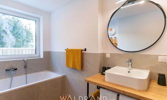 A modern bathroom with a bathtub and a sink on a wooden shelf. Large windows provide plenty of daylight and an inviting atmosphere.
