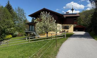 A cozy house surrounded by greenery, with a blue sky in the background. The path leads to the driveway of the house.