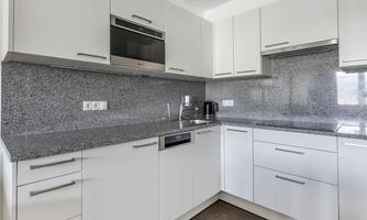 Modern kitchen with white cabinets and gray marble countertop. Equipped with modern appliances and plenty of light.