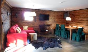 A cozy living space with wood paneling, red sofas, and a dining table. The room is bright and inviting, with a carpet and a television.