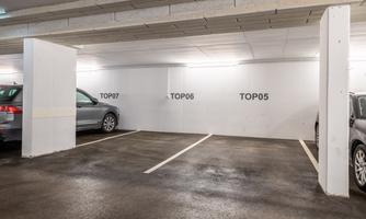 A parking garage with two parked cars. On the wall, the numbers TOP05, TOP06, and TOP07 are visible.